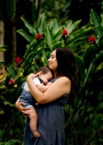 Mom holding baby in front of red ginger plant