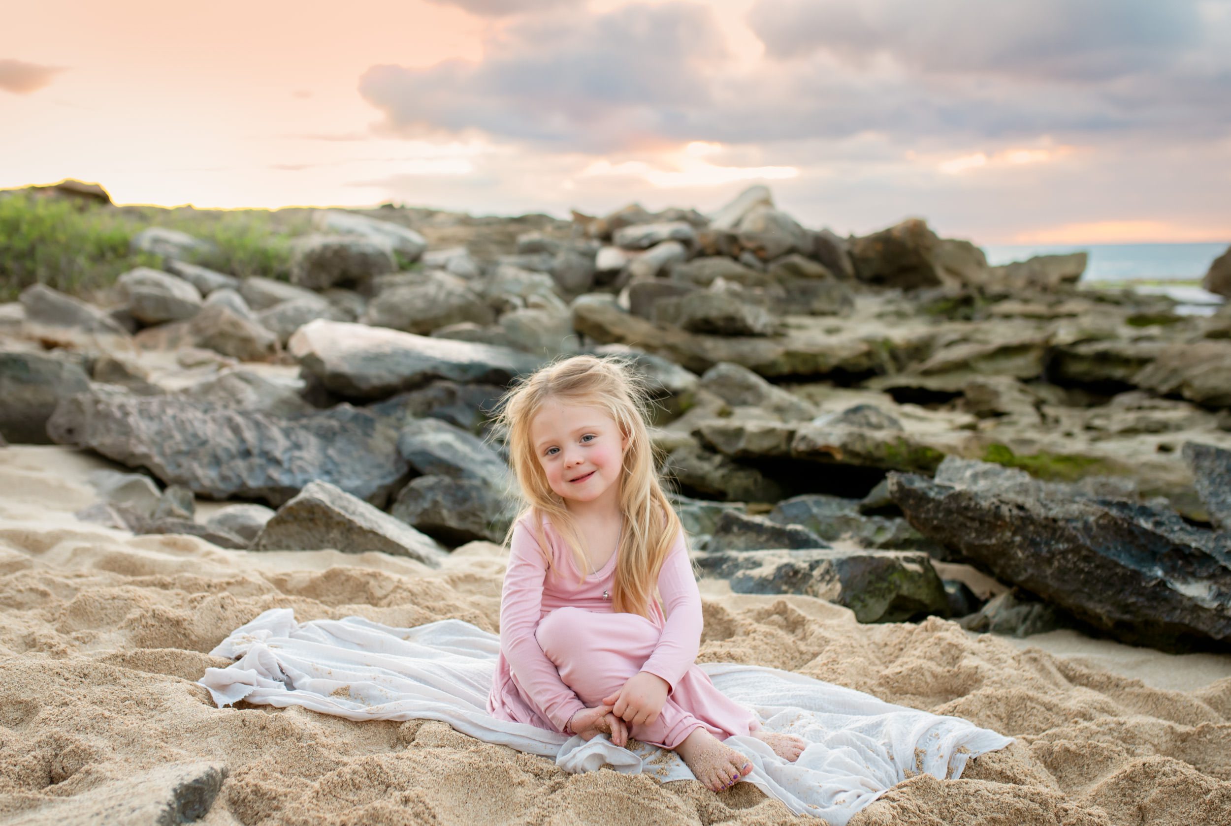 girl sitting on sand at sunset
