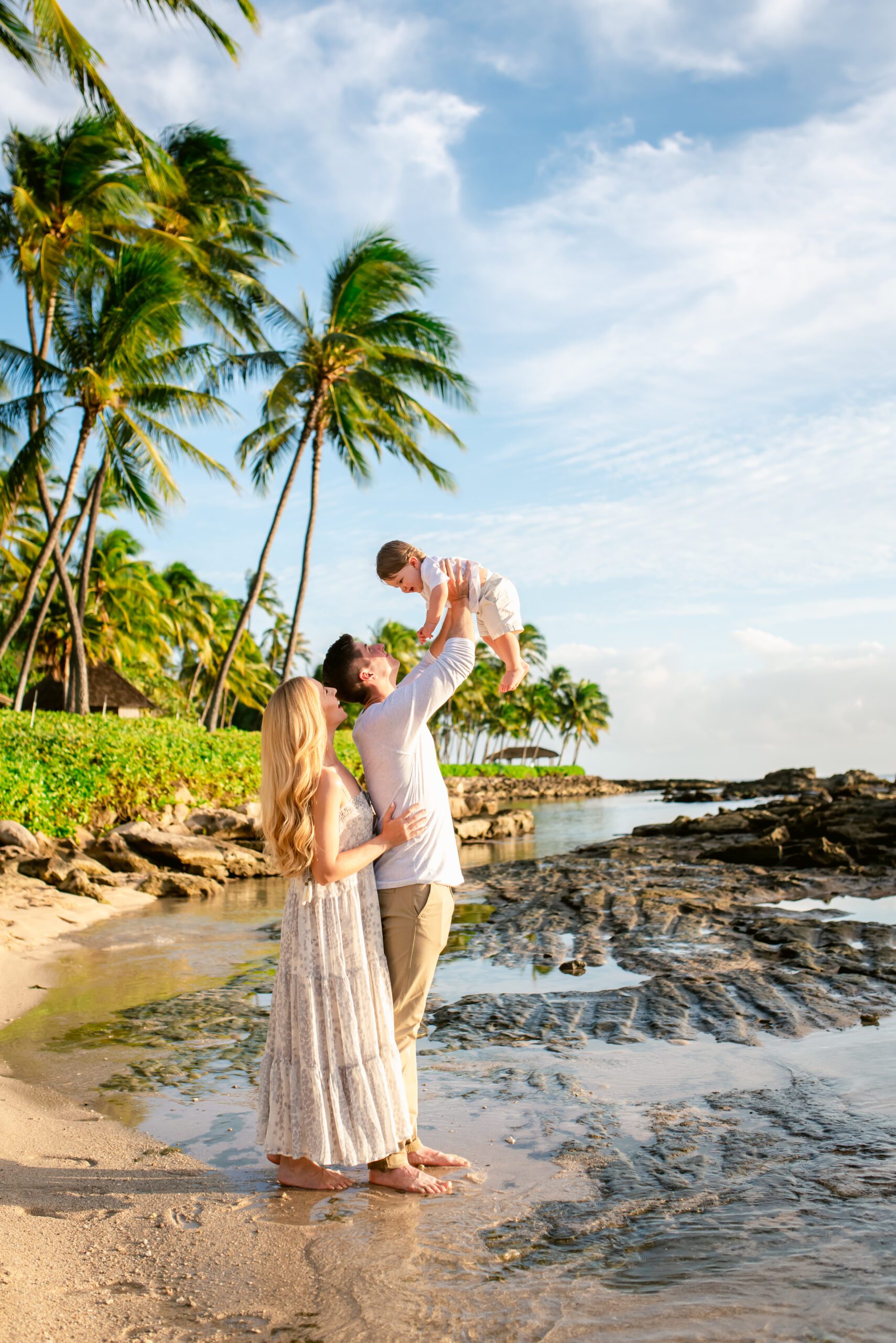 Family of three on a beach with palm trees and lava rocks