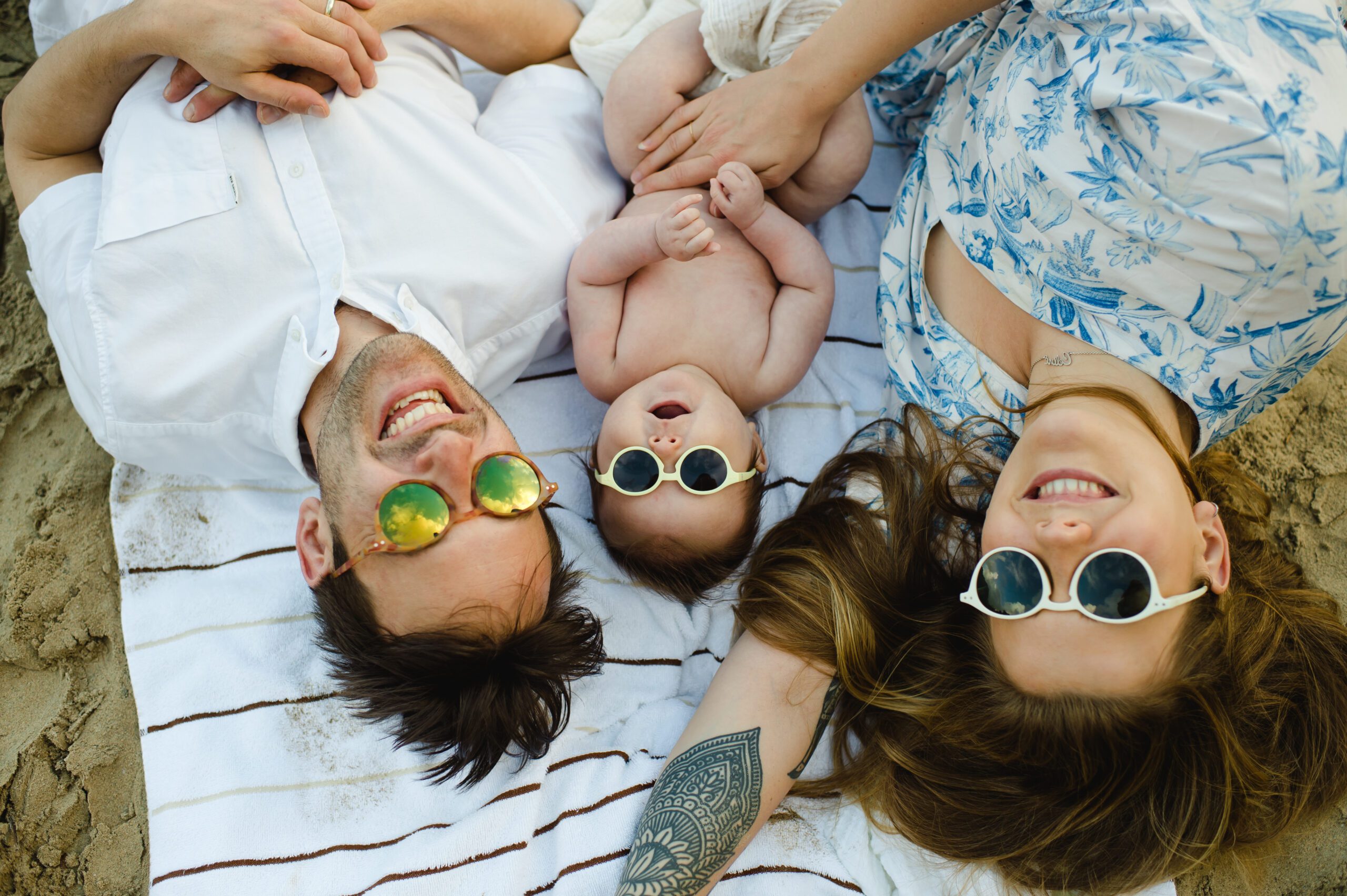 Young family with baby wearing sunglasses relaxing on beach towel with happy