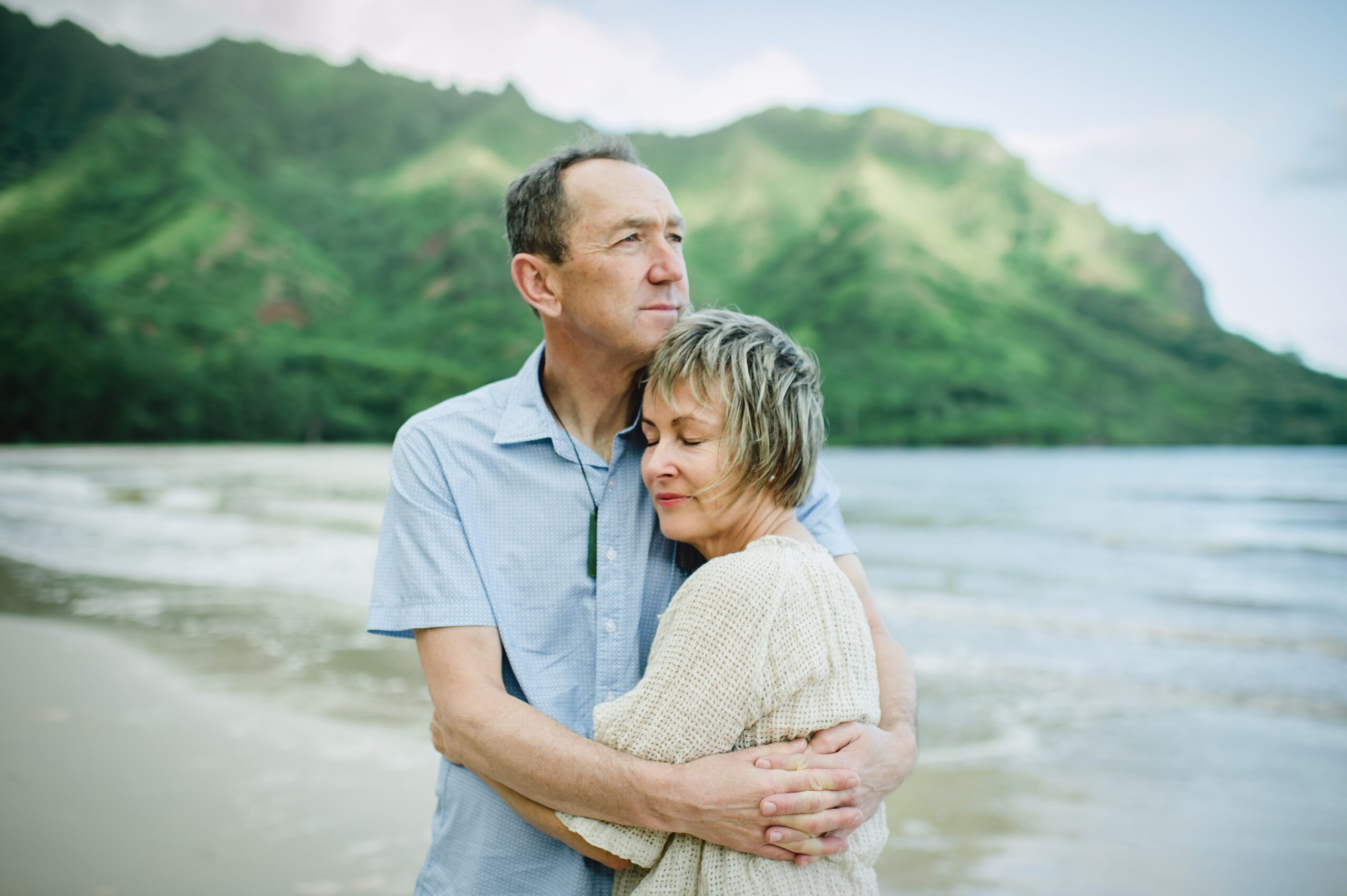 Elderly couple embracing lovingly on beach with ocean and mountains in the background